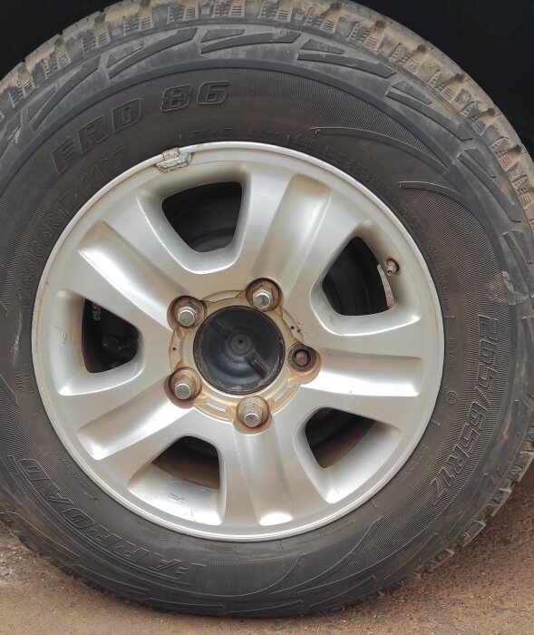 Närbild av Toyota Land Cruiser-fälg och däck på parkeringsplats, med tydliga bultar och små märken på fälgen.