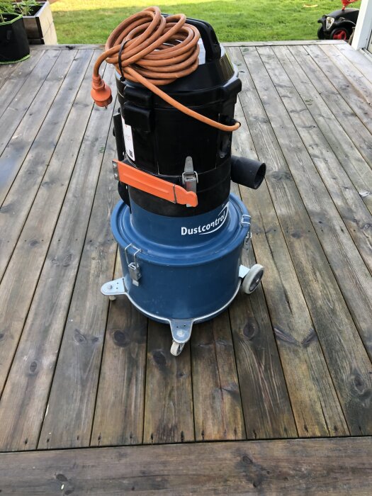En Dustcontrol DC1800 dammsugare med orange sladd på en träveranda.