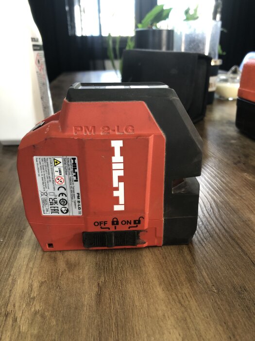 Grön laser Hilti PM 2LG står på ett bord med etiketter och text som beskriver funktioner.