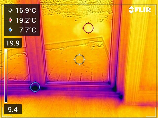Termografisk bild av ett fönsterområde som visar temperaturvariationer. Lägre temperaturer syns vid nederdelen av dörren, vilket kan indikera dålig isolering.