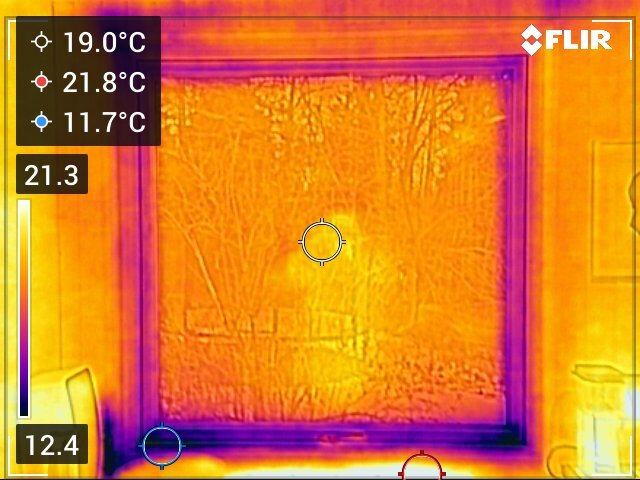 Värmekamera bild av fönster med temperaturskillnader; varmaste området inuti rummet och kallare runt fönsterkarmar, visar potentiella otätheter.
