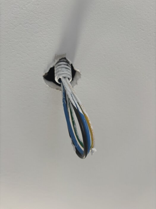 Elkablar hänger från hål i taket i en nybyggd lägenhet, förberett för installation av spotlights.