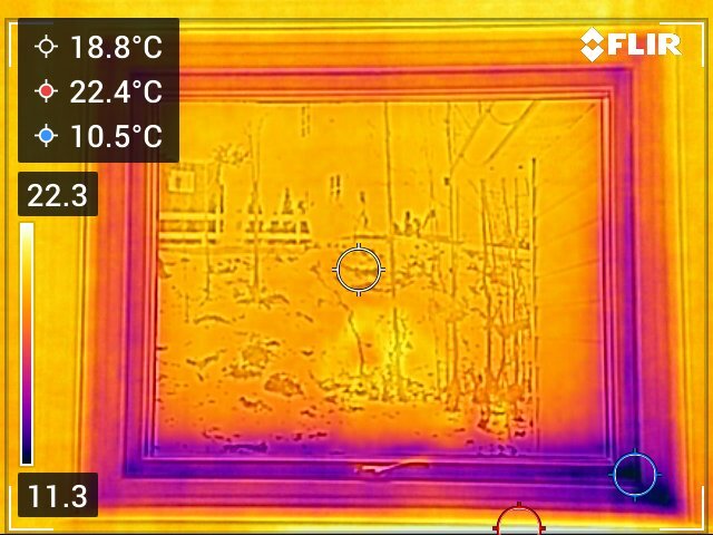 Termografisk bild av ett fönster som visar temperaturvariationer. Ljusa områden tyder på värmeförlust medan mörkare områden visar kallare zoner.