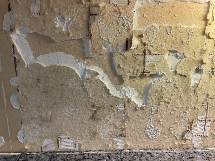 Skadad vägg efter borttagning av kakel med trasig gips och limrester synliga ovanför köksbänkens granitskiva.