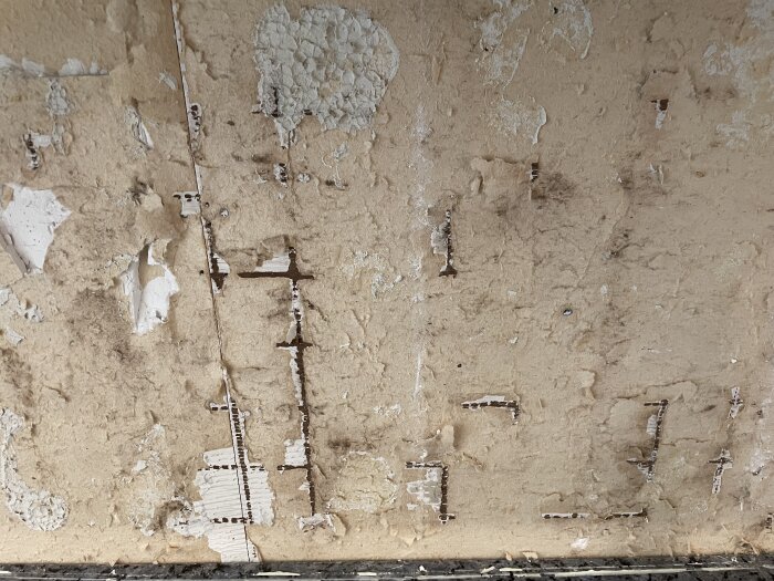 Skadad gipsskiva där kakel har tagits bort, visar avflagad yta med rester av lim och bitar av gipsskiva saknas.