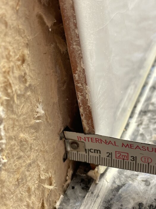 Mätsticka vid köksvägg där kaklet har tagits bort och gipsskiva delvis skadats.