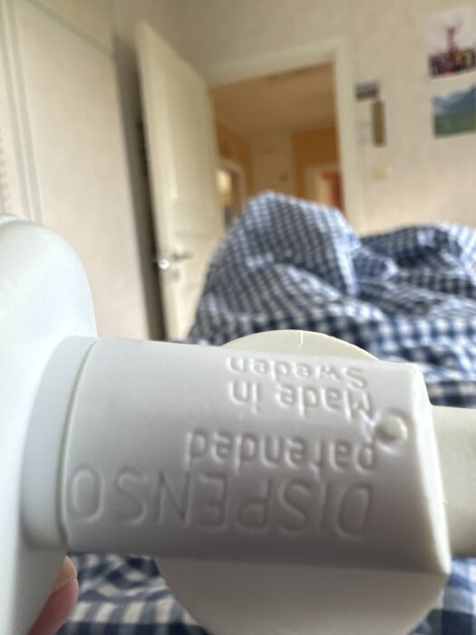 En vit plastrulle märkt "DISPENSO Patented Made in SWEDEN" och en trekant med siffran 07, mot en bakgrund av ett rum med öppen dörr.
