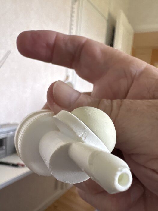 En hand håller en vit plastkomponent märkt "Dispenso Patented Made in SWEDEN" med en trekantssymbol och siffran 07.