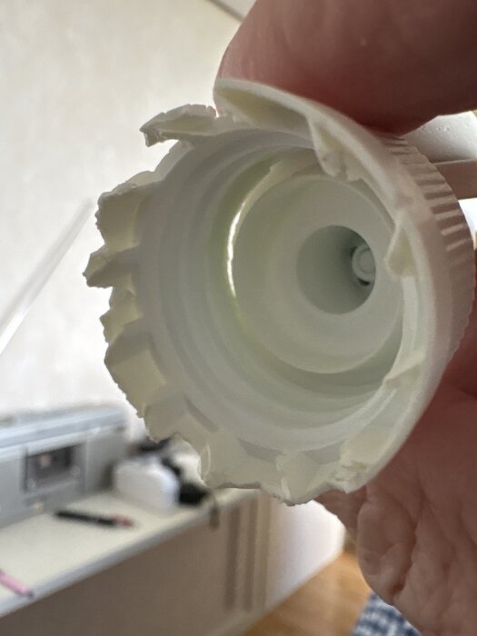 Trasigt vitt plastlock märkt Dispenso Patented, tillverkat i Sverige, med en trekant och numret 07.