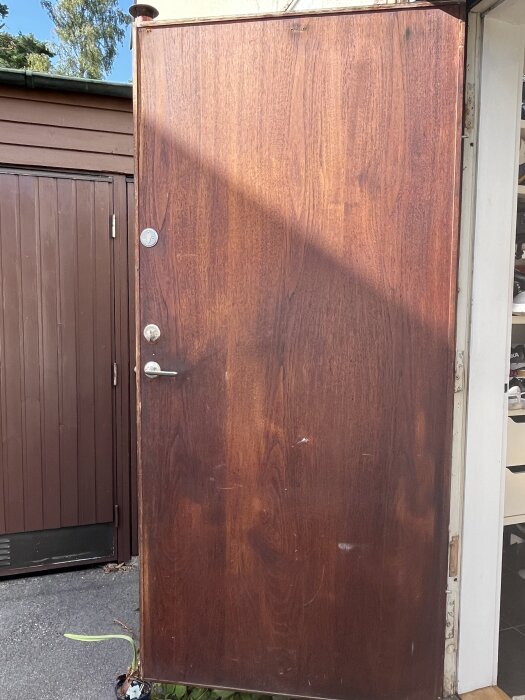 Dörr i teak från 60-talet, delvis slipad med synliga oljerester. Framsidan exponerad för dagsljus, med grannar runt hörnet.