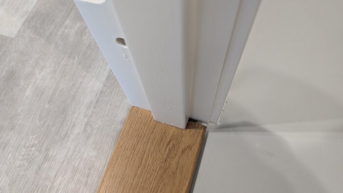 Vit dörrkarm med sned passform mot golvsockel av trä, med synlig springa som kan behöva fyllas med vit målarfog.
