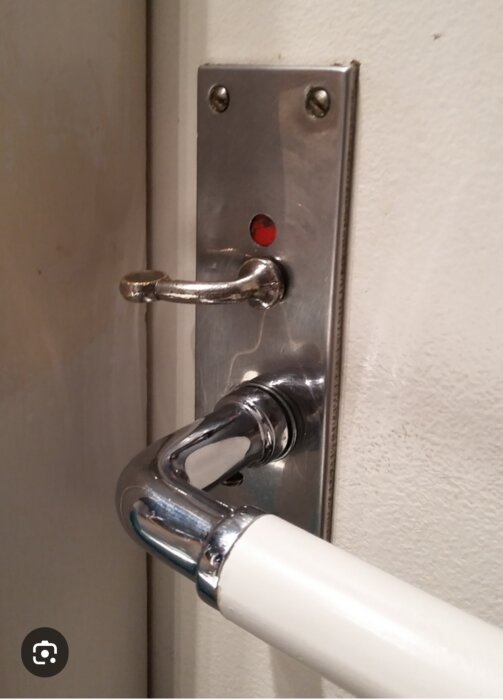 Metallhandtag med röd indikator på en dörr.