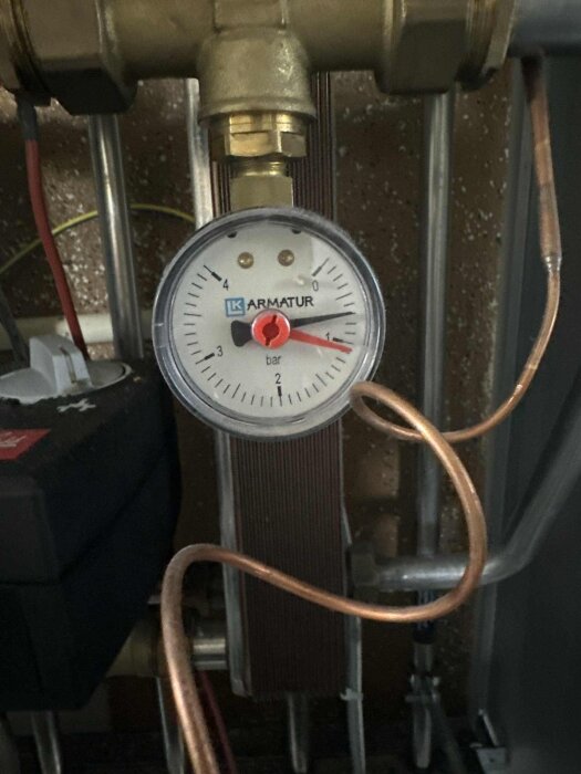 Manometer på fjärrvärmecentral visar trycket vid cirka 1,5 bar, omgiven av metallrör och kopparledningar.