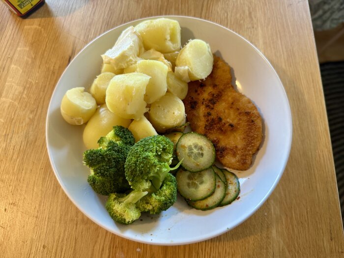 Tallrik med kokt potatis, broccoli, snitzel och skivad gurka.