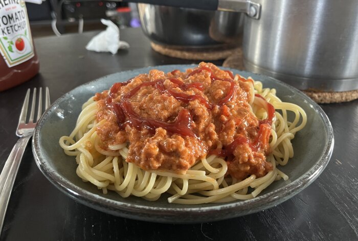 Spaghetti med chorizoköttfärssås och ketchup på en tallrik, med en kastrull och ketchupflaska i bakgrunden.