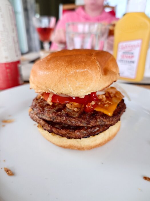 Frysburgare med ost och tomat på en tallrik, ketchup- och senapsflaskor i bakgrunden.