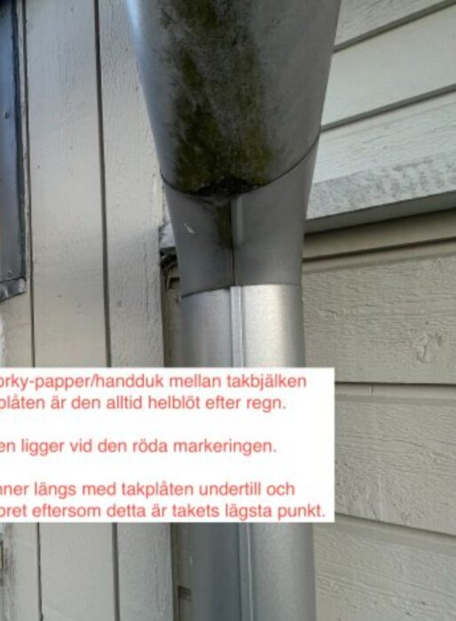 Nedre del av stuprör med mörk missfärgning vid böjen, fäst vid väggen, med synlig text som beskriver en vattenläcka.