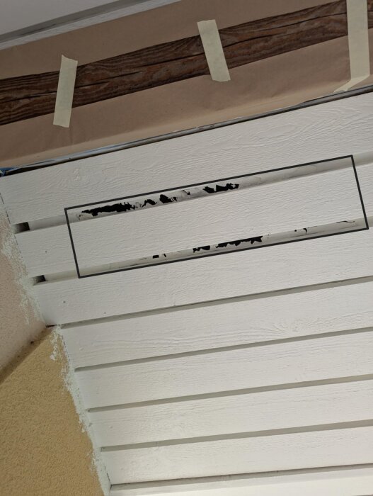 Brädor under takfot med rödmarkerad plast ovanför. Svartmarkerat område visar trasig plast med färgskador. Tape och pappersskydd syns ovanför.