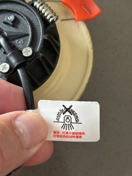 Närbild på undersidan av en spotlight med en etikett som visar ett varningsmärke och kinesisk text.
