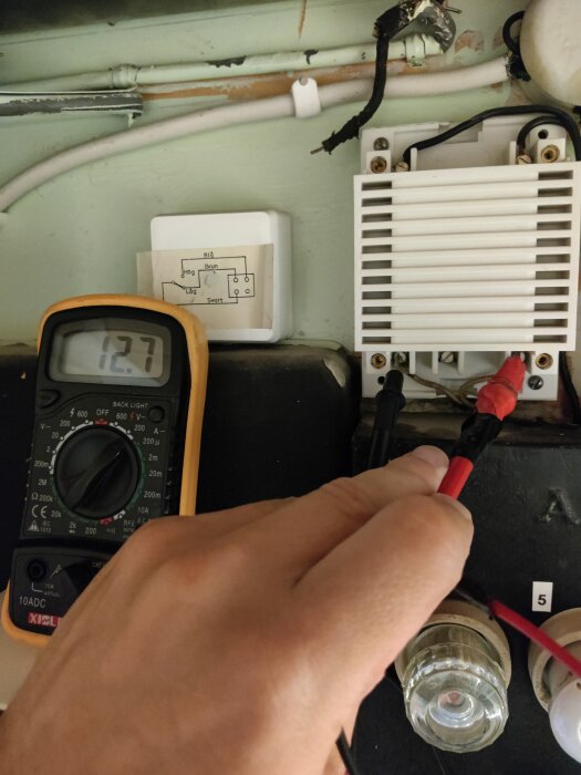 Multimeter visar 12,7V i en elektrisk koppling, undersökt för att avgöra om dörrklockan fungerar med specifik spänning på 6-12V.