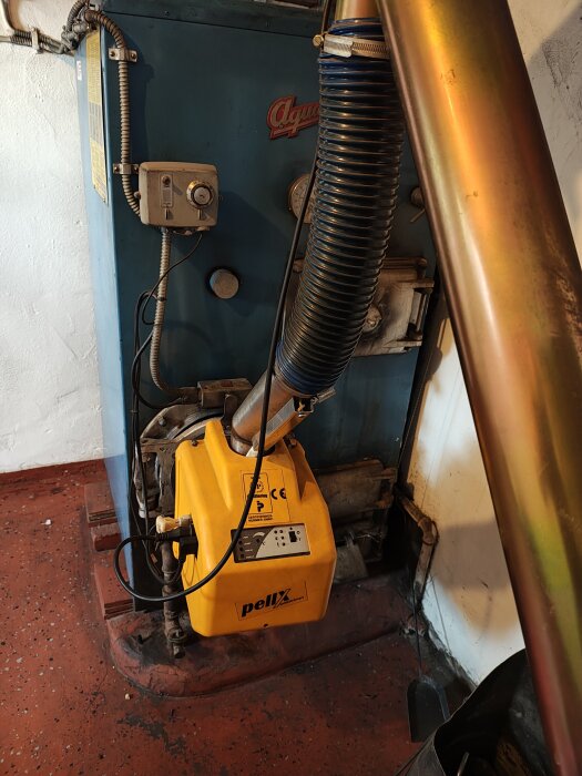 En gammal oljepanna med en installerad pelletsbrännare av märket pellx kmp px21, fotograferad i ett källarutrymme.