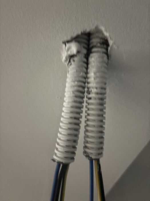 Två vita korrugerade rör som går genom taket med blå och gula elektriska kablar synliga undertill.