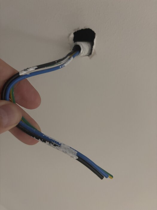 En hand håller i flera elektriska kablar som kommer ut ur ett hål i en vit vägg.