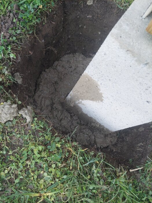 Betongplint i marken omgiven av grovbetong och jord, med gräs runt omkring.