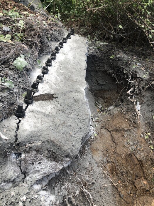 Spräckta stenar med kilar insatta i rad, omgivna av jord och växtlighet, visar pågående stenbrytning.