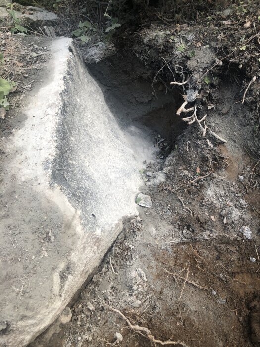 Stor sten har delats och flyttats med hjälp av kilar och borrmetod. Synliga sprickor och rötter intill stenen i marken.