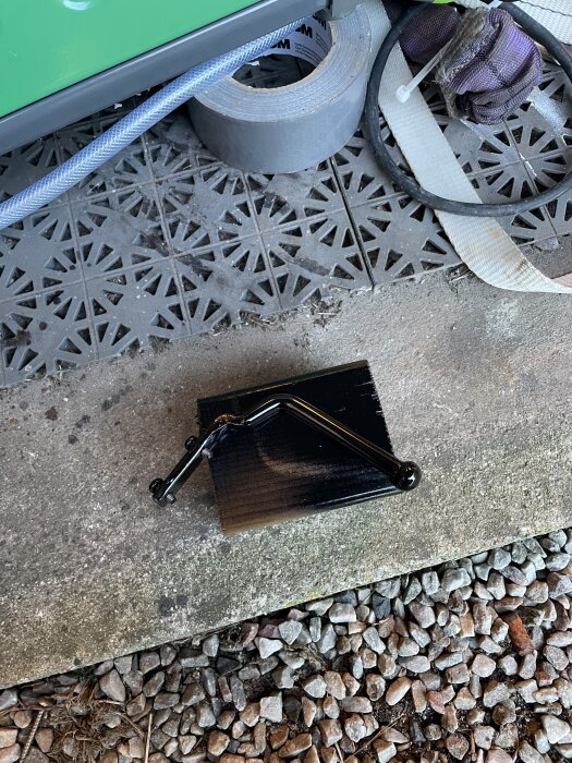 Svart metallkonstruktion på en betongyta, omgivet av grus och verktyg.