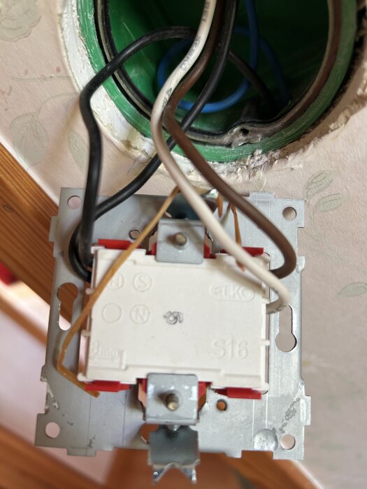 Gamla elanslutningar i en kronbrytare monterad i väggen, med synliga kablar och delar av kopplingsdosan.