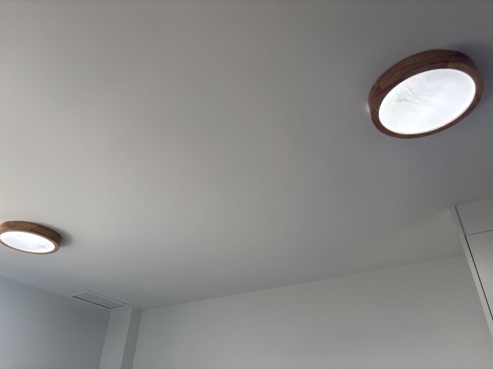 Två runda taklampor med träkant monterade i ett vitt tak.