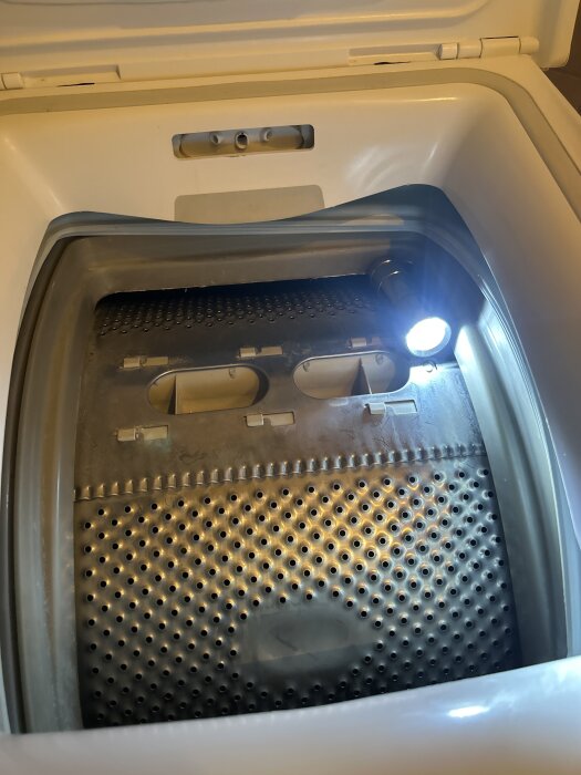 Toppmatad Whirlpool-tvättmaskin med öppen lucka och ficklampa riktad mot trumman, fokus på monteringsproblemet med gummilisten.