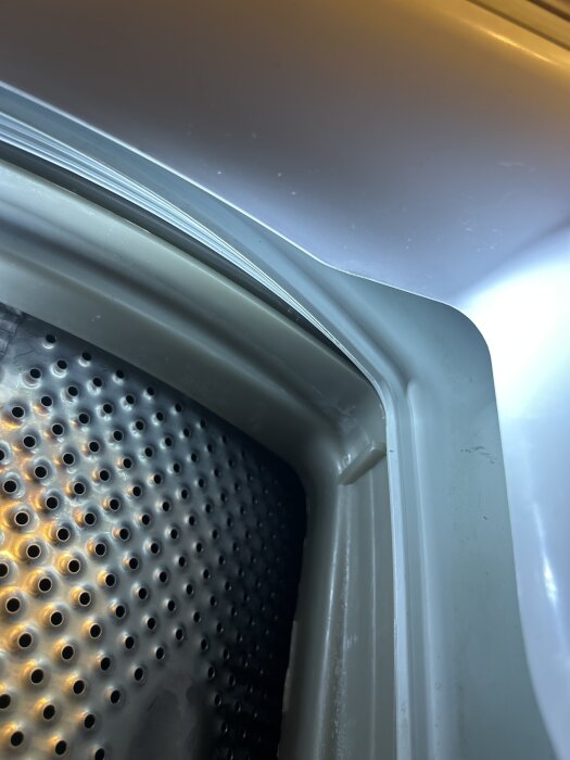 Närbild på insidan av en toppmatad Whirlpool-tvättmaskin som visar problemområde för montering av gummilist i ett av maskinens hörn.