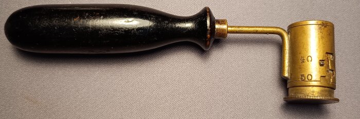 Äldre ställbart krutmått i metall, med svart handtag, för användning vid handladdning av ammunition.