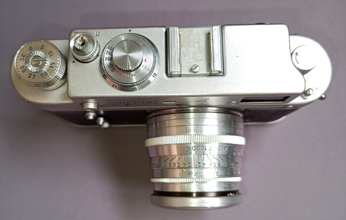 Vintage kamera ovanifrån, silverfärgad med objektiv och inställningsvred, troligen en äldre modell från Sovjetunionen.