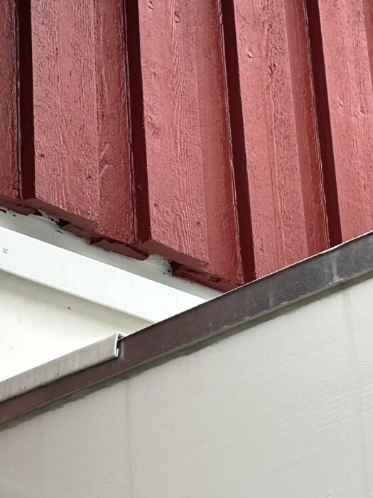 Röd träpanel och vit plåt på ett tak där brädor kapats för att få plats med ny plåt under vindpappen.