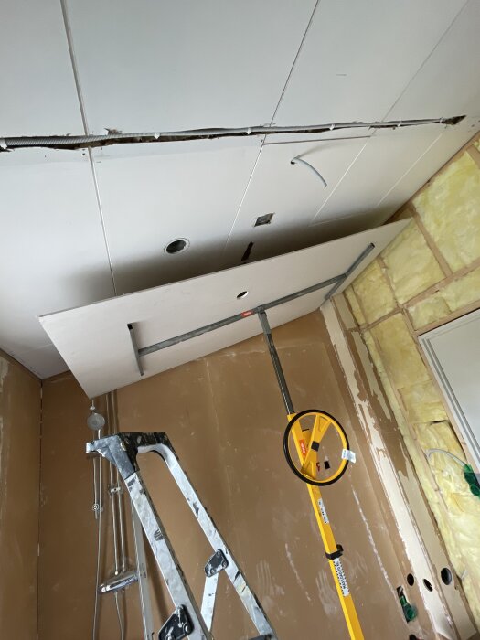 Stege och verktyg mot delvis öppnat tak med masonitskivor och isolering synlig, förbereder installation av gipsplattor i 80-talshus.