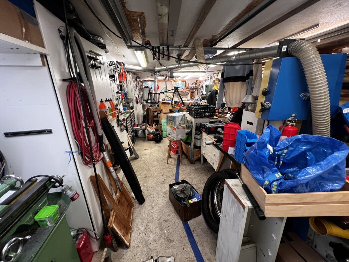 Verkstad full med verktyg och material, inklusive slangar, förvaringsbehållare och en träsvarv, med en smal gång genom rummet.