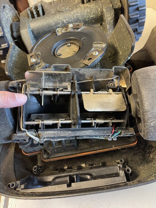 Bild på insidan av en gräsklippare med fokus på trasig svart kabel vid metallbleck, som kan påverka laddningen.