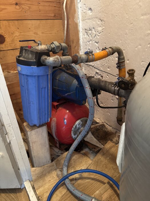 Vattenpump och filter i ett pumphus med olika kopplingar och rör.
