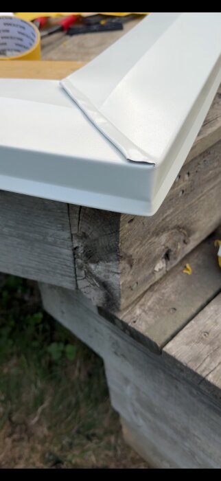 Närbild på ett hörn av en vit plåt på en trästomme utomhus, med verktyg och material i bakgrunden.
