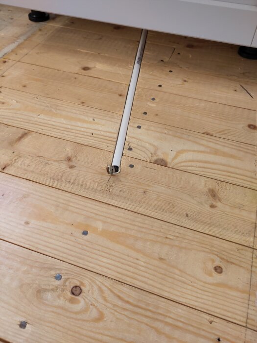 PVC-rör för eldragning ligger på råspontgolv, med tre elkablar inuti. Förberett för golvskikt ovanpå, synlig närbild av rör och kablar.