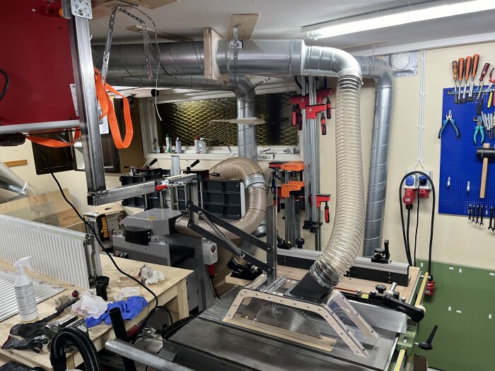 Verkstad med nyinstallerat klingskydd och utsug ovanför bordssåg, tillverkat av plywood och polykarbonat, kopplat till tak med justerbar arm.