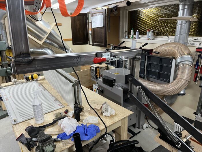 Verkstad med custom byggt klingskydd vid bordssåg, tillverkat av plywood och polykarbonat, med ett utsugssystem och justerbar stödarm.