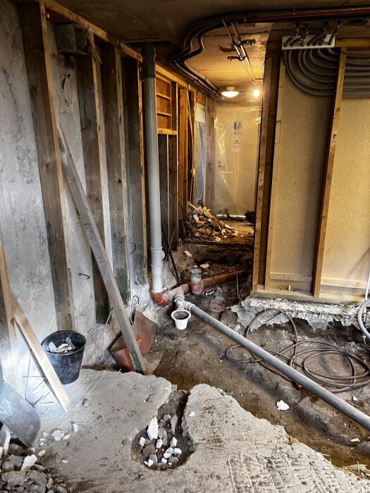 Renovering av tvättstuga med öppnade väggar, rörsystem och byggmaterial på golvet. Ljusslinga och plastdraperi i bakgrunden.