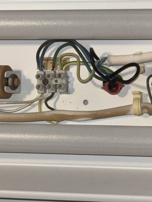 Lysrörslampa med kablar och anslutningar synliga, inklusive grön, svart, neutral och jordkabel, kopplade till en plint.