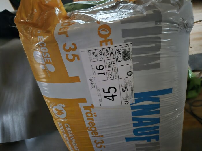 Förpackning av Knauf Träregel 35 isoleringsmaterial, etikett synlig med detaljer som 45 mm tjocklek och brandsäkerhet, används i husrenovering.