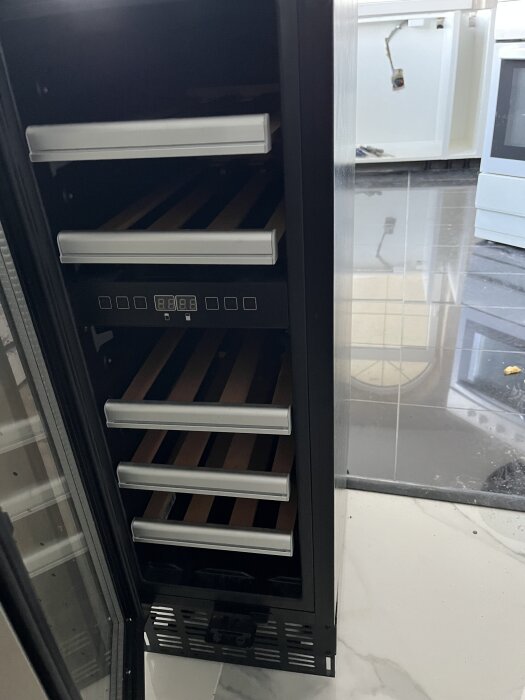 Öppen vinkyl med flera hyllor och digital display, del av kök syns i bakgrunden.